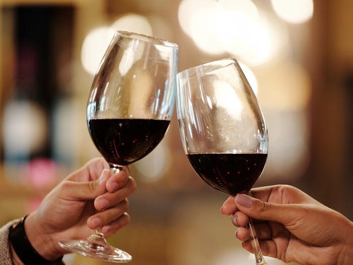 Close-up of two people toasting red wine glasses in a restaurant setting.